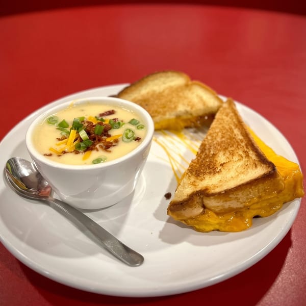 Creamy soup topped with bacon and green onions, served with two grilled cheese sandwich halves.