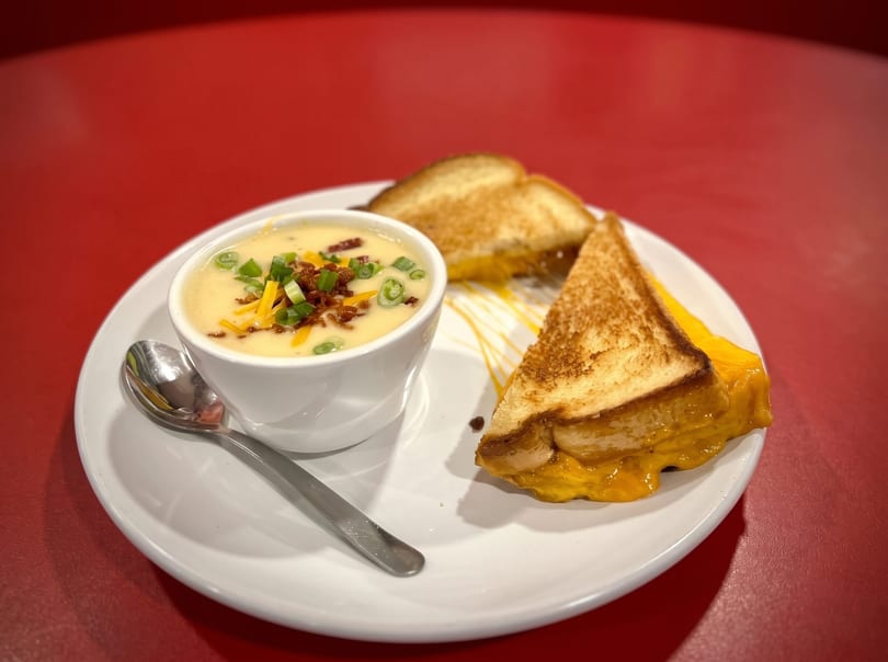 Creamy soup topped with bacon and green onions, served with two grilled cheese sandwich halves.