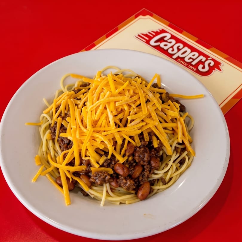 Casper's chili spaghetti with beans and shredded cheddar cheese on a white plate.