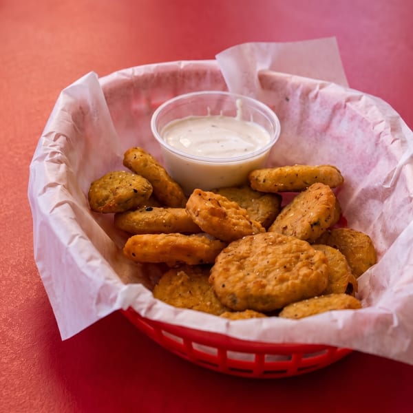 A red plastic basket filled with crispy fried pickles and a side of ranch dressing on a red table.