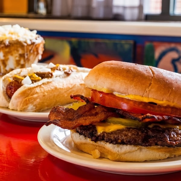 A bacon cheeseburger, hot dog, and chili cheese fries on a red table.