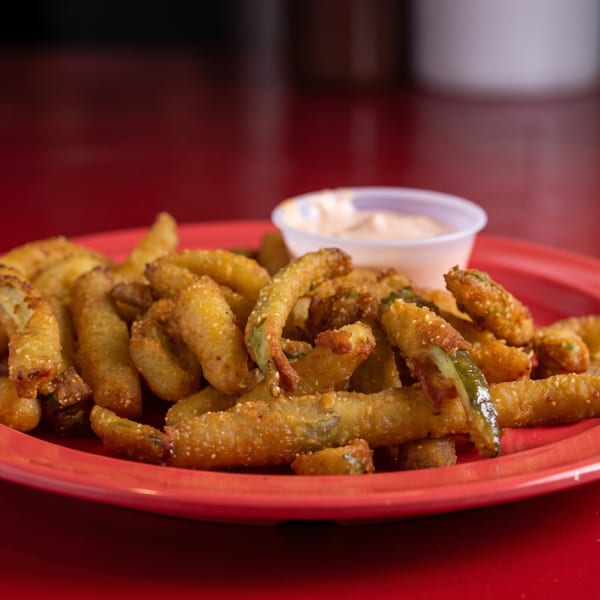 Crispy fried pickle spears on a red plate with a side of dipping sauce.
